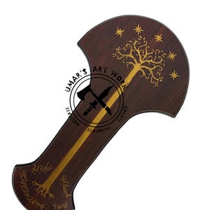 May include: A wooden axe handle with a gold stripe down the center. The top of the handle is shaped like a shield with a gold tree and stars on a dark brown background. The text "UMAR'S ART WORK" is printed in a circle on the handle. The text "INNOVATE CREATE" is printed on the handle. The text "3rd Realm" is printed on the handle.