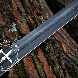 May include: A black sword with etched inscriptions, resting on a textured wood surface. The sword's blade is dark, and the handle is not visible. The image includes a white circular logo with the text "UMAR'S ART WORK".