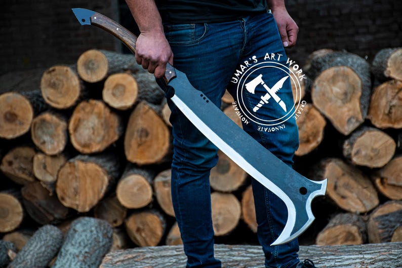 K&ouml;nnte beinhalten: Eine gro&szlig;e, schwarz-silberne Klinge mit Holzgriff wird vor einem Stapel Holzscheite gehalten. Die Klinge hat ein gebogenes Design und eine scharfe Kante. Der Griff ist braun und hat ein dunkles Ende. Das Logo "UMAR'S ART WORK" ist sichtbar.