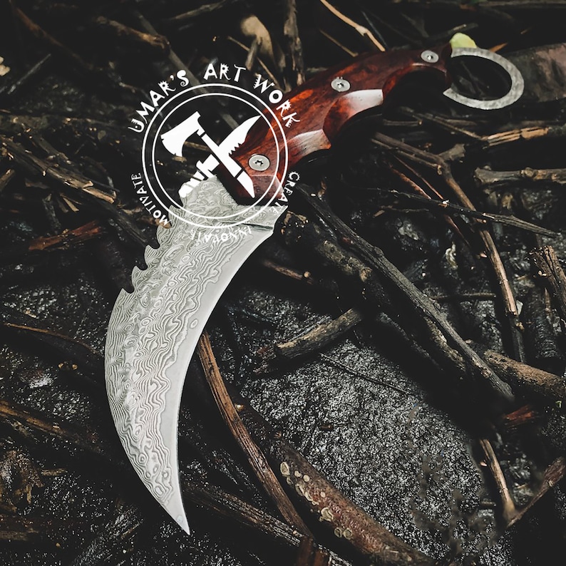 Puede incluir: Un cuchillo de hoja curva con una hoja de acero estampada y un mango de madera. El cuchillo tiene un anillo para el dedo y est&aacute; sobre un fondo oscuro y texturizado con el texto "UMAR'S ART WORK".
