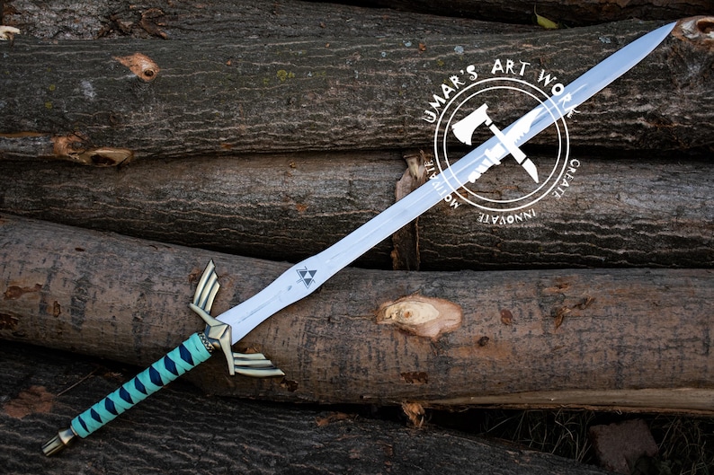 May include: A silver-colored sword with a teal and gold handle, resting on a pile of logs. The sword features a triangular emblem and gold accents. The handle is wrapped in a teal and black pattern. The image includes a circular logo with text.