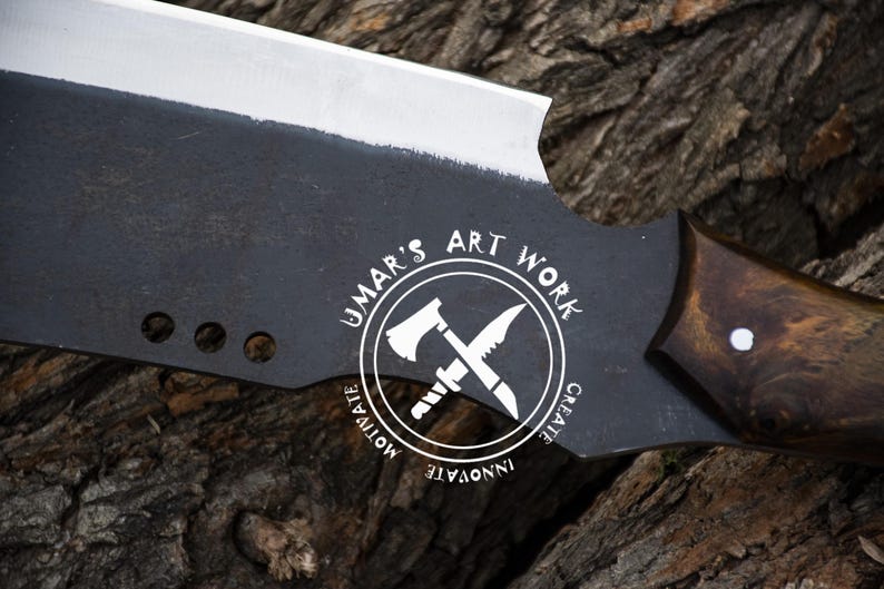 K&ouml;nnte beinhalten: Ein gro&szlig;es, schwarzes Metallbeil mit einer silbernen Klinge und einem dunklen Holzgriff. Das Beil hat eine einzigartige Form und tr&auml;gt den Text "UMAR'S ART WORK" in einem kreisf&ouml;rmigen Logo. Die Klinge hat drei L&ouml;cher in der N&auml;he des Griffs.