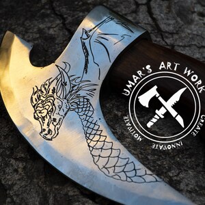May include: A metal axe head with a dark wooden handle featuring an etched dragon design on the blade. A circular logo is visible on the blade with the text UMAR'S ART WORK, MOTIVATE, CREATE, INNOVATE, and an icon of an axe and a knife crossed.