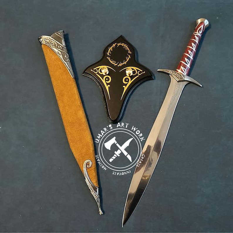 May include: A sword, sheath, and shield set. The sword has a silver blade and a red and silver handle. The sheath is tan with silver accents. The shield is black with gold detailing. The set is displayed on a dark surface. The text "UMAR'S ART WORK" is visible.