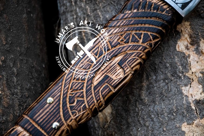 May include: Close-up of a wooden axe handle with intricate carvings. The handle is dark brown with black accents and features a repeating pattern of geometric shapes. The text "UMAR'S ART WORK" is visible on the handle.