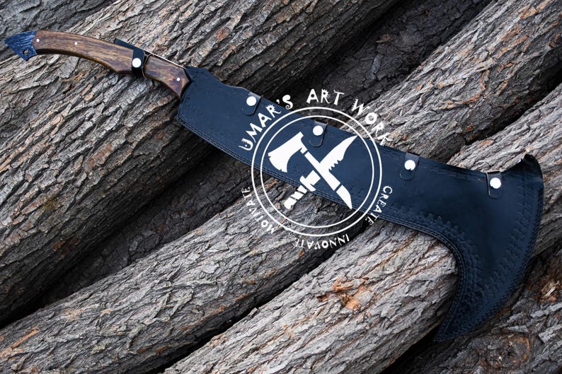 K&ouml;nnte beinhalten: Eine handgefertigte Axt mit Holzgriff und schwarzer Klingenh&uuml;lle. Die Axt hat einen dunklen Holzgriff und eine schwarze Klingenh&uuml;lle mit dem Text "UMAR'S ART WORK". Die Axt liegt auf einem Stapel Holzst&auml;mme.