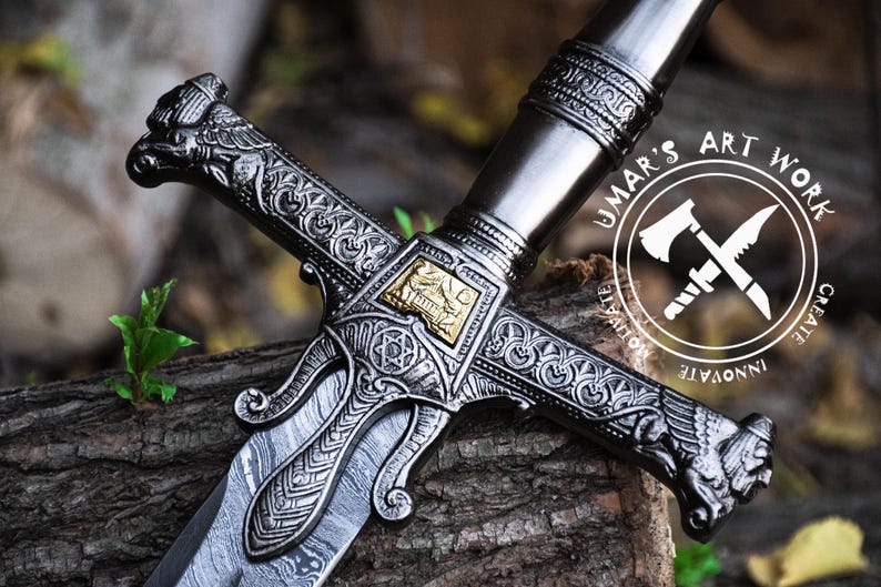 May include: A detailed, intricately carved sword with a silver blade and gold accents. The hilt features a cross guard with ornate designs and a decorative pommel. The sword is resting on a wooden surface. The image includes the text "UMAR'S ART WORK CREATE INNOVATE MOTIVATE".