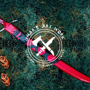 May include: A red and black sword with a leather scabbard. The scabbard has a black and white logo with the text "UMAR'S ART WORK CREATE INNOVATE MOTIVATE".