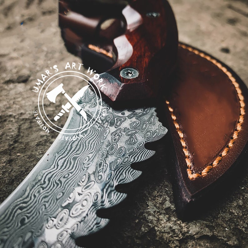Puede incluir: Primer plano de un cuchillo personalizado con una hoja estampada y un mango de madera. El cuchillo est&aacute; parcialmente enfundado en una funda de cuero marr&oacute;n con costuras visibles. La hoja tiene un patr&oacute;n ondulado &uacute;nico. El texto "UMAR'S ART WORK" es visible.