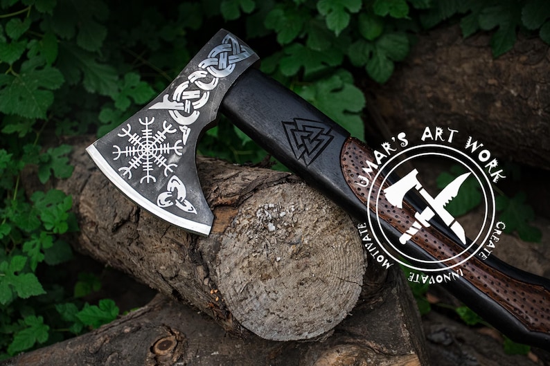 Op de afbeelding: Een zwarte en zilveren bijl met een houten steel. De bijlkop is versierd met een Keltisch knoopontwerp en een Viking-symbool. De steel is versierd met een Viking-symbool en de woorden "UMAR'S ART WORK CREATE INNOVATE MOTIVATE".