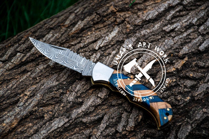 May include: A folding pocket knife with a patterned steel blade and a blue and brown wooden handle. The handle has the words "Innovate, Motivate, Create" and "Umar's Art Work" on it.