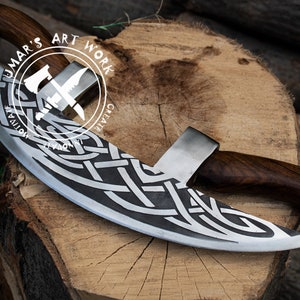 May include: A curved blade with a dark wood handle and a silver metal edge featuring an intricate etched Celtic knot pattern. The blade is marked with a circular logo containing the text UMAR'S ART WORK, MOTIVATE, CREATE, and INNOVATE.