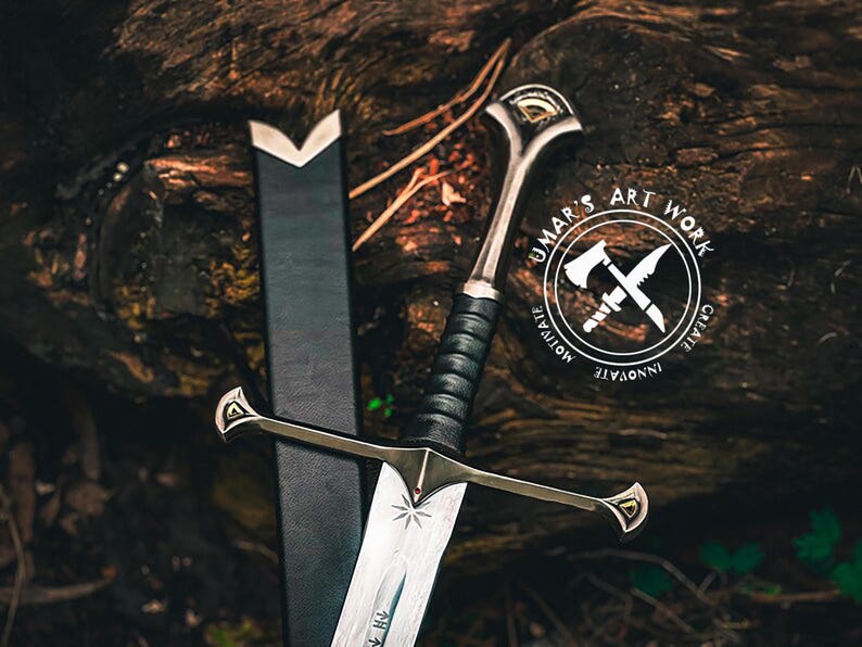 May include: A detailed image of a sword with a black handle and silver blade, resting against a dark sheath. The sword features a decorative hilt and crossguard. The image includes a logo that says "UMAR'S ART WORK" with the words "MOTIVATE", "INNOVATE", and "CREATE".