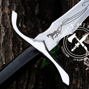 May include: A silver sword with a black handle and a decorative design on the blade. The design includes a horse pulling a carriage and the text "UMAR'S ART WORK".