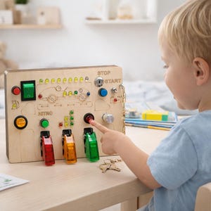 Op de afbeelding: Een houten activiteitenbord met diverse interactieve elementen, waaronder knoppen, schakelaars en speelgoedauto's. Het bord bevat de woorden "STOP", "START" en "NITRO". Een kind interacteert met het bord en drukt op een rode knop.