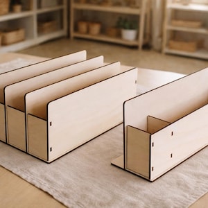 Könnte beinhalten: Zwei helle Schreibtisch-Organizer aus Holz mit glatter Oberfläche. Ein Organizer verfügt über drei vertikale Fächer zur Dokumentenaufbewahrung, während der andere ein Ablagefach mit einer hohen Rückwand und einem kleinen Trennelement ist.