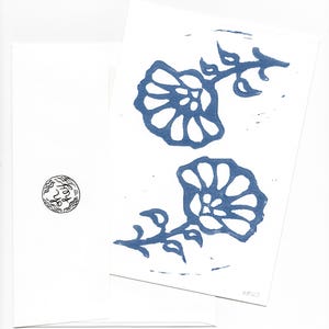 May include: Two greeting cards with blue floral block prints on white paper. One card features two flower designs with stems and leaves. The other card has a small circular design. The cards are displayed against a white background.