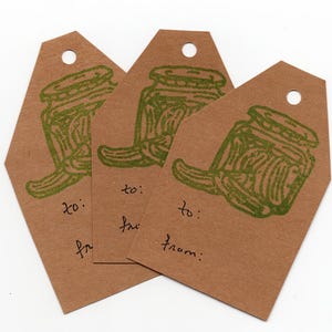 Puede incluir: Tres etiquetas de regalo marrones con un sello verde de un tarro de pepinillos. Cada etiqueta tiene las palabras "a:" y "de:" escritas en ellas.