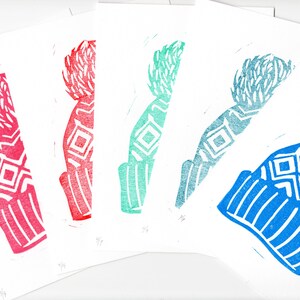 May include: A series of linocut prints depicting a winter hat design in different colours. The prints show a hat with a bobble and geometric patterns in shades of red, teal, blue, and turquoise. The prints are on white paper.