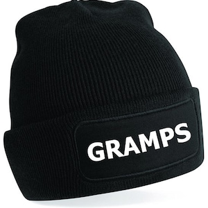 Puede incluir: Gorro de punto negro con un parche negro en la parte delantera que dice "GRAMPS" en letras blancas.