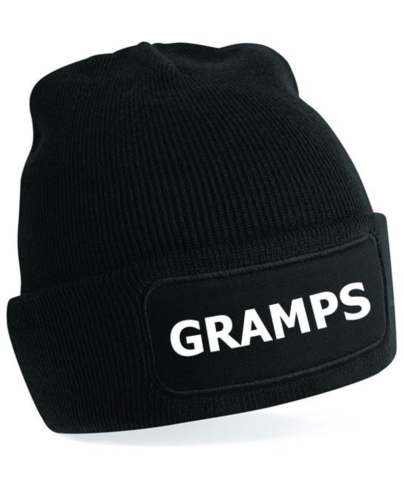 Puede incluir: Gorro de punto negro con un parche negro en la parte delantera que dice "GRAMPS" en letras blancas.