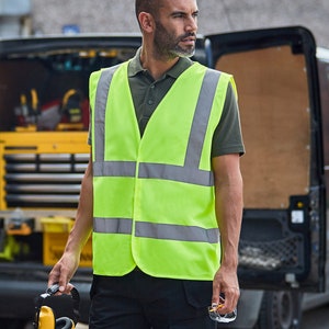 K&ouml;nnte beinhalten: Eine Person tr&auml;gt eine neongr&uuml;ne Sicherheitsweste mit reflektierenden silbernen Streifen. Die Weste hat einen Rei&szlig;verschluss und wird &uuml;ber einem dunkelgr&uuml;nen Poloshirt getragen.