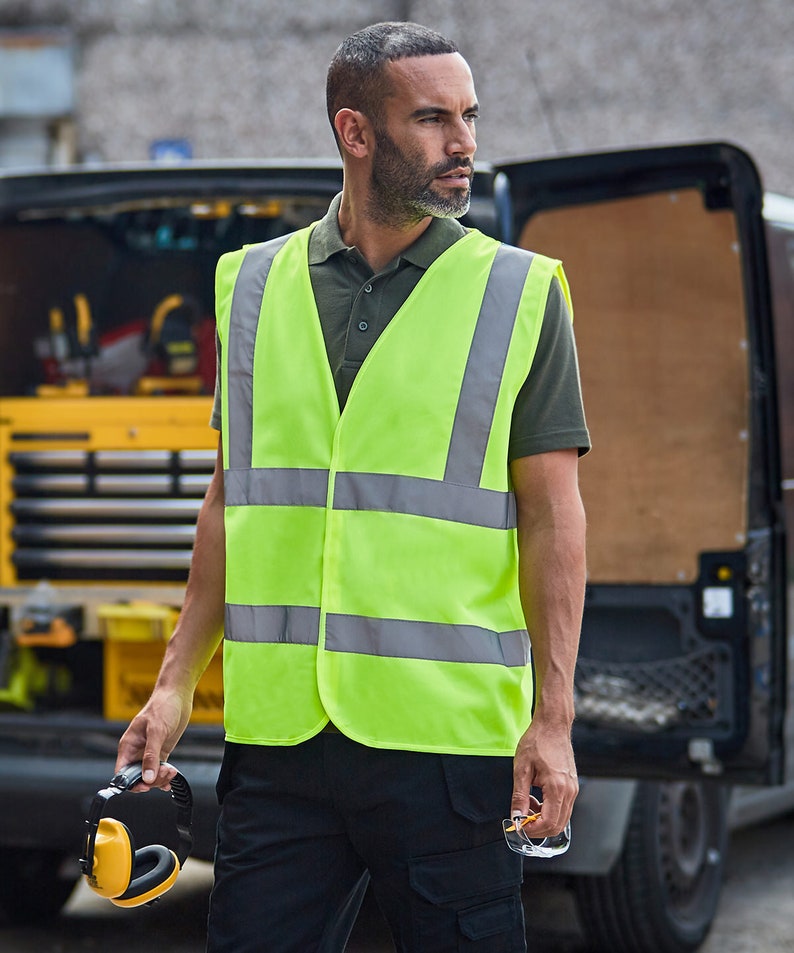 K&ouml;nnte beinhalten: Eine Person tr&auml;gt eine neongr&uuml;ne Sicherheitsweste mit reflektierenden silbernen Streifen. Die Weste hat einen Rei&szlig;verschluss und wird &uuml;ber einem dunkelgr&uuml;nen Poloshirt getragen.