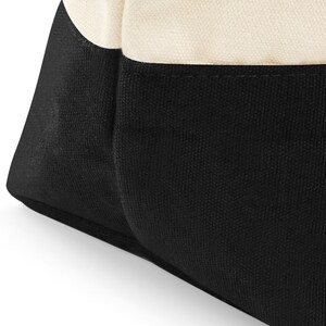 May include: A black and white canvas tote bag with a black bottom and a white top. The bag is made of a sturdy canvas material and has a simple, classic design.