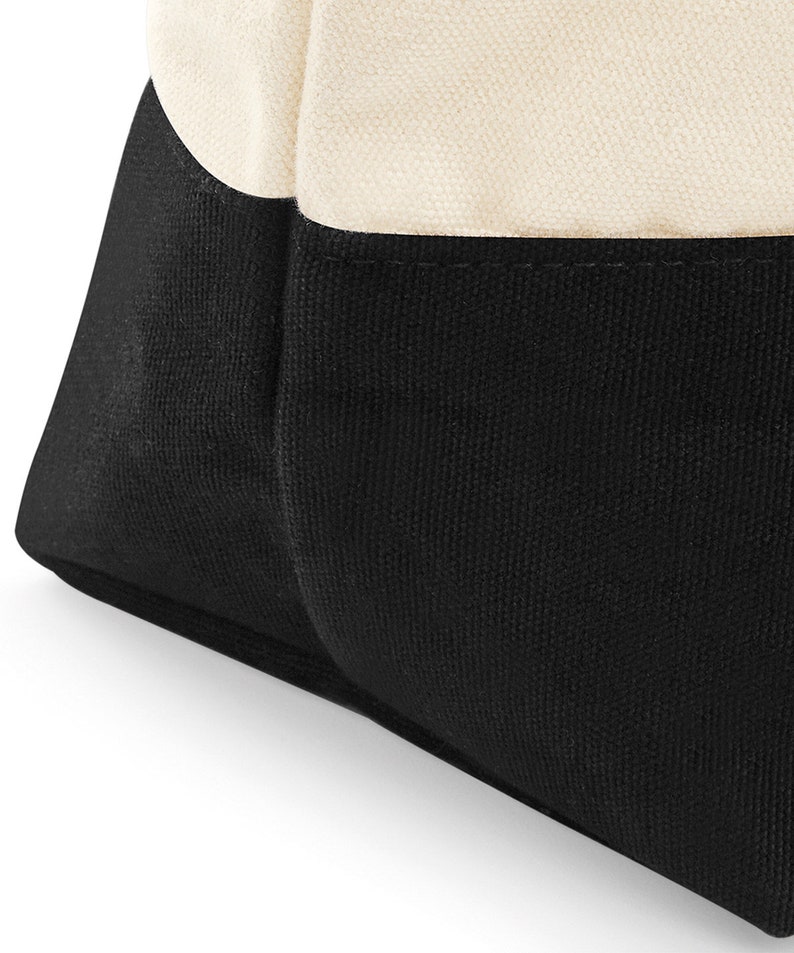 May include: A black and white canvas tote bag with a black bottom and a white top. The bag is made of a sturdy canvas material and has a simple, classic design.