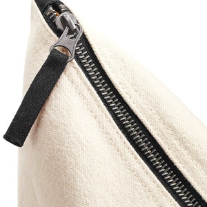 May include: Close-up of a white canvas zipper pouch with a black zipper and pull tab.