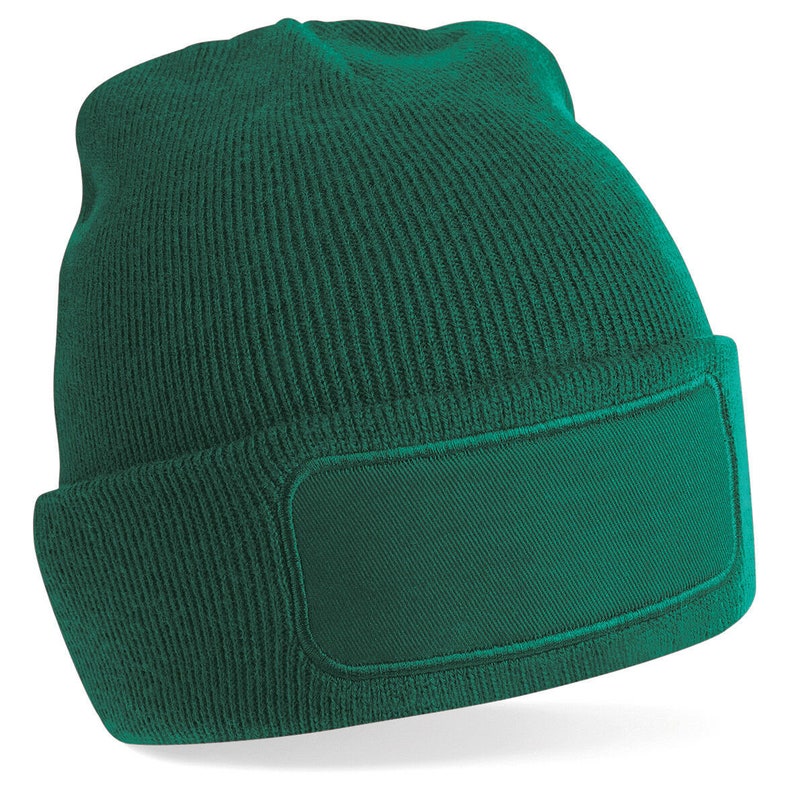 Puede incluir: Un gorro de punto verde oscuro con un parche rectangular grande en la parte delantera. El parche tambi&eacute;n es verde oscuro.