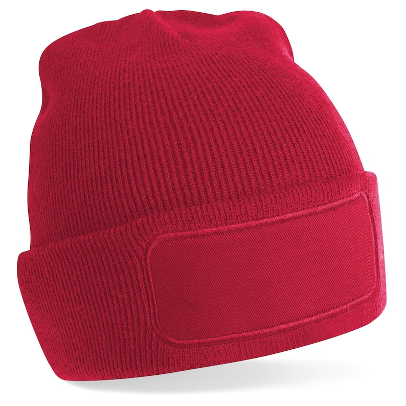 Puede incluir: Un gorro de punto rojo con un parche rectangular en blanco en la parte delantera.