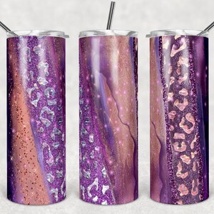Pode incluir: Três copos de aço inoxidável com um design de glitter roxo e rosa. Os copos têm um acabamento metálico e são decorados com um padrão de redemoinho de glitter roxo, rosa e dourado.