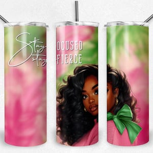 May include: A tumbler with a pink and green floral background features a portrait of a woman with dark hair. The tumbler has the words "Stay Focused, Stay Fierce" in white script. A silver straw is included.
