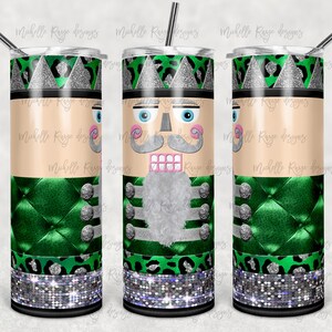 Op de afbeelding: Een groene en zilveren tumbler met een notenkrakerontwerp. De tumbler heeft een luipaardprint en een zilveren glitterband rond de onderkant. De tumbler is versierd met een notenkrakergezicht, een groen en zilveren jasje en een groen en zilveren hoed.