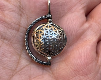 May include: A silver pendant with a flower of life design. The pendant is attached to a silver chain and has a small loop at the top for attaching to a necklace.