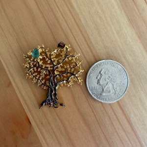May include: A gold tree of life pendant with a green gemstone in the center. The pendant is about the size of a quarter.