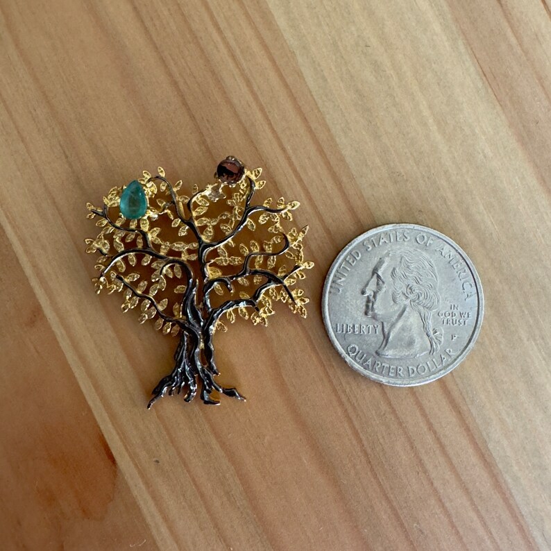 May include: A gold tree of life pendant with a green gemstone in the center. The pendant is about the size of a quarter.
