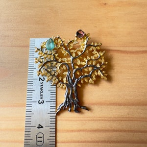 May include: A gold and silver tree of life pendant with green and pink gemstones. The pendant is about 2.5 inches tall and is measured against a ruler.