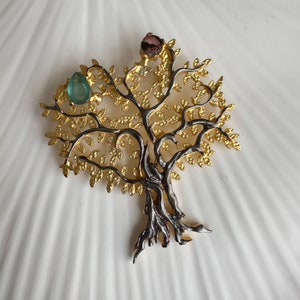 May include: A gold and silver tree of life pendant with green and pink gemstones. The pendant is detailed with intricate branches and leaves.