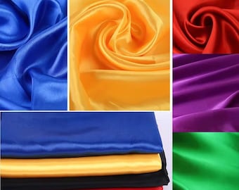 May include: A collection of satin fabric pieces in various solid colors including blue, yellow, red, purple, and green. The fabric displays a smooth, reflective surface with soft folds and drapes, shown both as individual swatches and stacked.