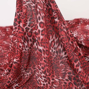 May include: Red and black leopard print fabric. The fabric has a sheer, lightweight appearance. The leopard spots are a deep red color with black outlines and white centers. The fabric is draped, showing the pattern's flow.