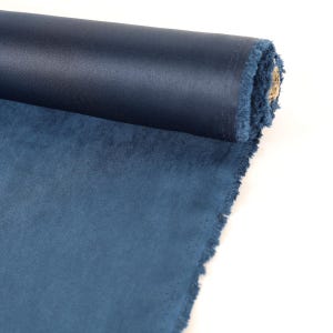 May include: A roll of dark blue fabric with a slightly textured surface. The fabric is rolled up and has a frayed edge.