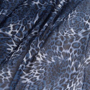 May include: Close-up of a blue and white leopard print fabric. The fabric has a sheer, mesh-like texture with a pattern of dark blue and white spots. The fabric is draped, creating folds and shadows.