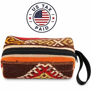 Könnte beinhalten: Eine rechteckige, gewebte Tasche mit einem schwarzen Reißverschluss und einem schwarzen Griff. Die Tasche hat ein geometrisches Muster in Braun-, Orange-, Gelb- und Rottönen. Der Text "US TAX PAID" ist darüber gedruckt.