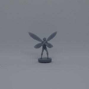 May include: A gray miniature figurine of a fairy with wings outstretched, standing on a round base.