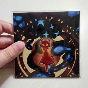 Op de afbeelding: Vierkante kunstdruk met een gestileerde figuur in een rode mantel en koptelefoon, tegen een donkere achtergrond met blauwe en gouden accenten. Het ontwerp bevat sterren en wervelende patronen, wat een kosmisch thema creëert.