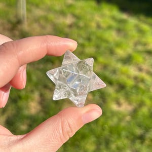 Op de afbeelding: Een helder kwartskristal in de vorm van een zespuntige ster, ook bekend als de Ster van David of Merkaba. Het kristal is gefacetteerd en heeft een gladde, gepolijste afwerking.