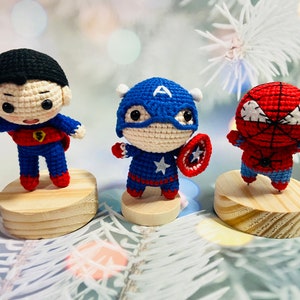 May include: Three crocheted superhero figurines: Superman, Captain America, and Spiderman. Each figurine is standing on a wooden base.