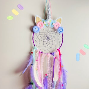 K&ouml;nnte beinhalten: Ein lila und wei&szlig;er Traumf&auml;nger mit einem Einhornhorn und Blumenschmuck. Der Traumf&auml;nger hat Federn und Perlen, die von ihm herabh&auml;ngen.